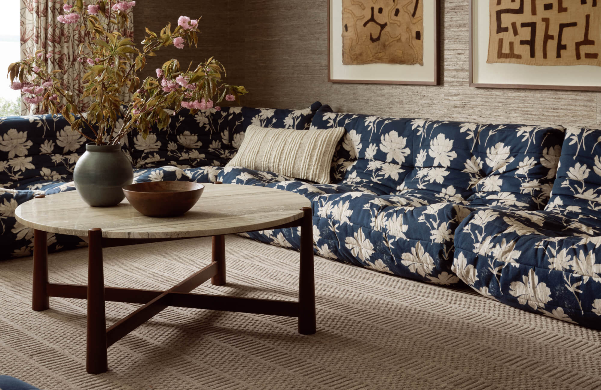 Plush sectional sofa in navy with bold white floral print, paired with a round travertine coffee table on a textured beige rug.