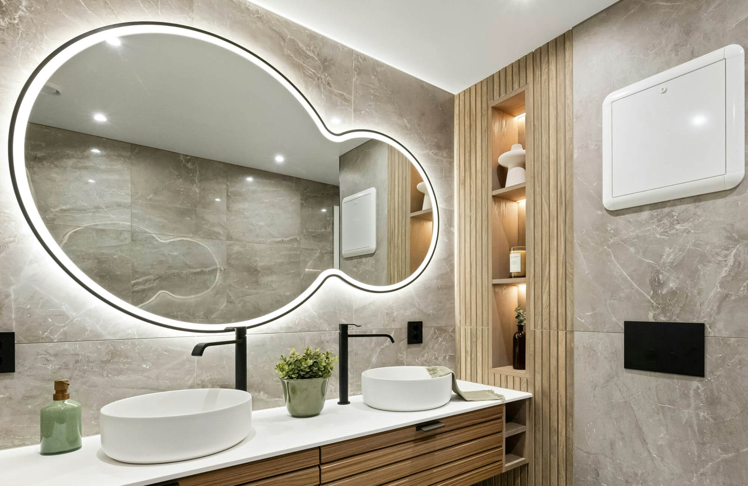 Modern bathroom mirror in an irregular organic shape with LED backlighting enhances the marble wall and adds a sleek, contemporary touch to the vanity space.