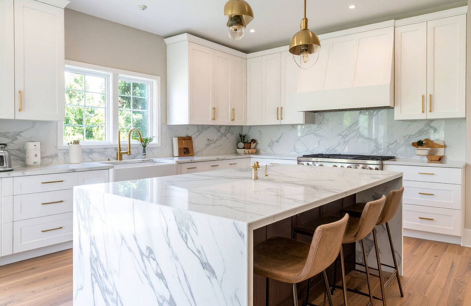 Bright kitchen with Calacatta marble waterfall island, white cabinetry, and warm brass pendants creating a refined, timeless look.