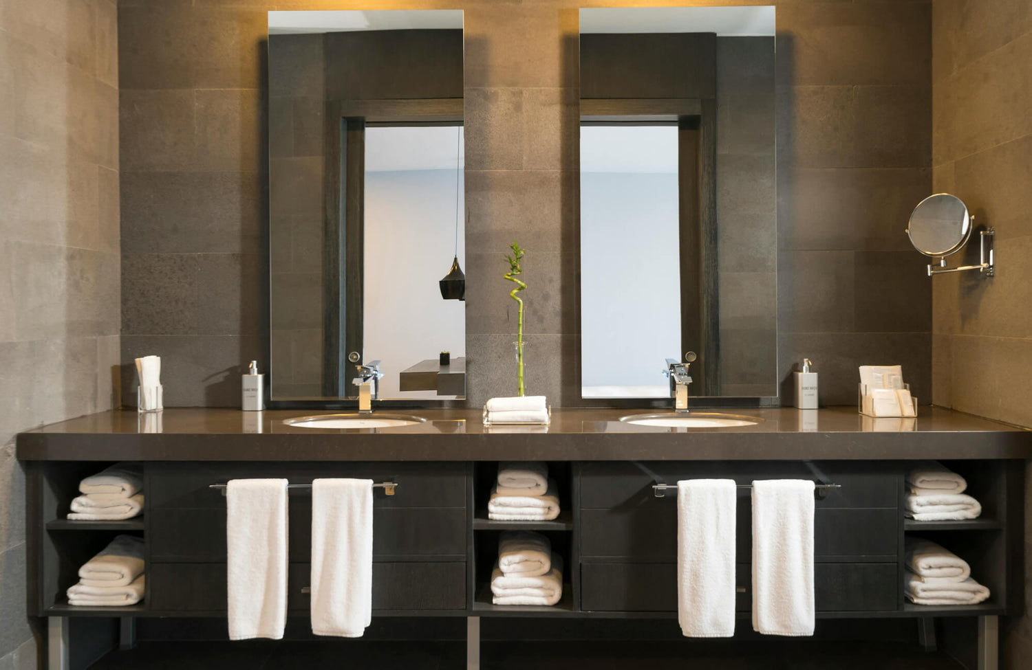Modern bathroom with dual rectangular mirrors above a sleek dark vanity, featuring neatly arranged white towels and minimalist décor for a refined, spa-like atmosphere.