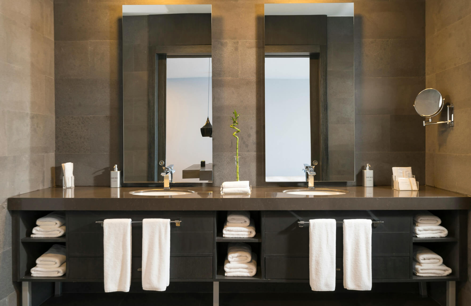 Modern bathroom with dual rectangular mirrors above a sleek dark vanity, featuring neatly arranged white towels and minimalist décor for a refined, spa-like atmosphere.