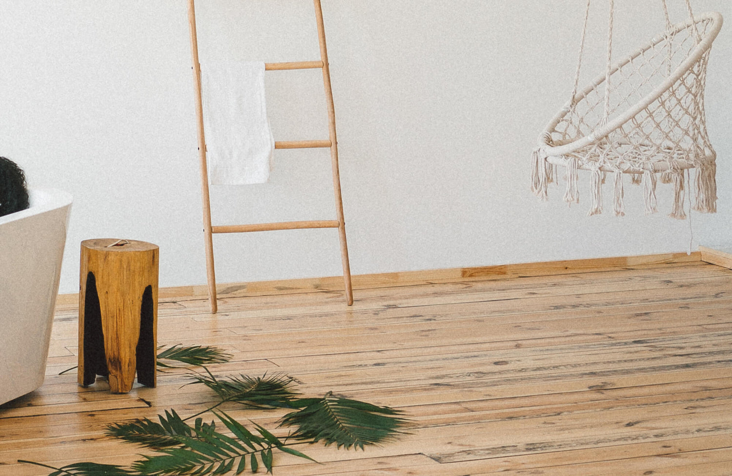 Wood flooring bathroom design featuring light natural wood planks, a freestanding tub, woven hanging chair, and minimalist decor with warm, spa-like ambiance.