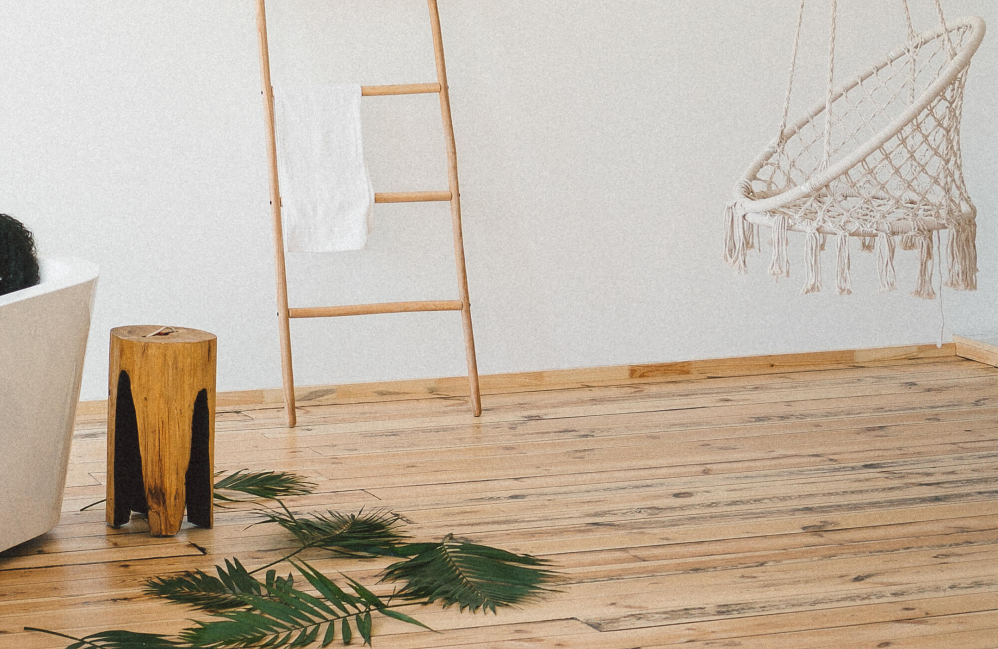 Wood flooring bathroom design featuring light natural wood planks, a freestanding tub, woven hanging chair, and minimalist decor with warm, spa-like ambiance.