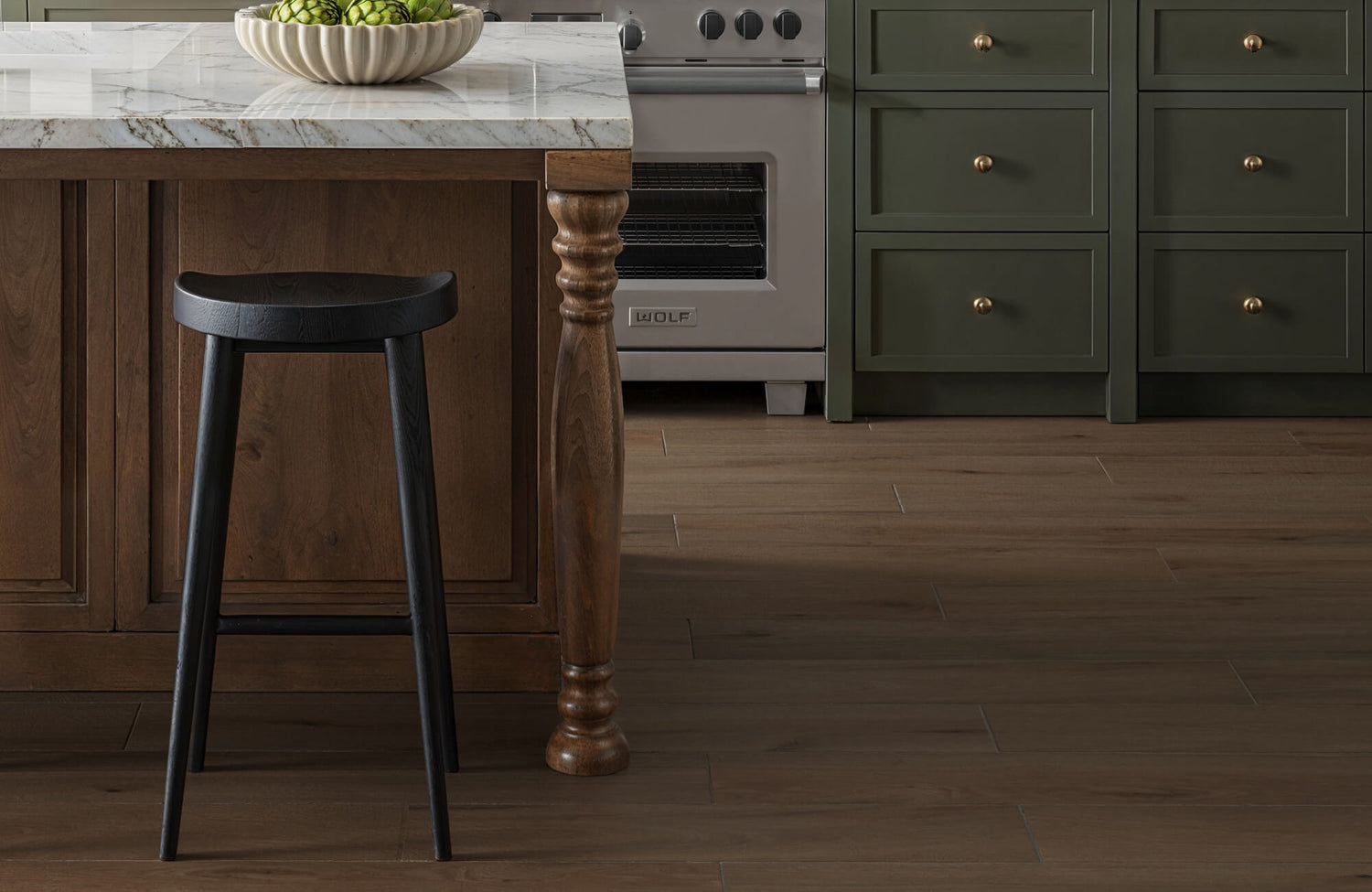 Warm-toned wood look tile in a kitchen with marble countertops and dark green cabinets