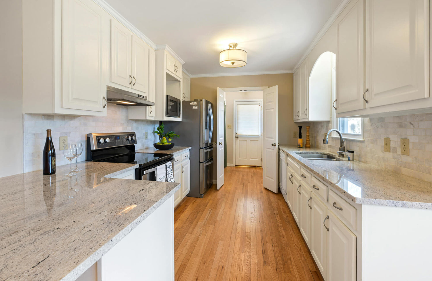 Bright galley kitchen with white cabinets, granite counters, and a simple ceiling light illuminating the narrow layout.