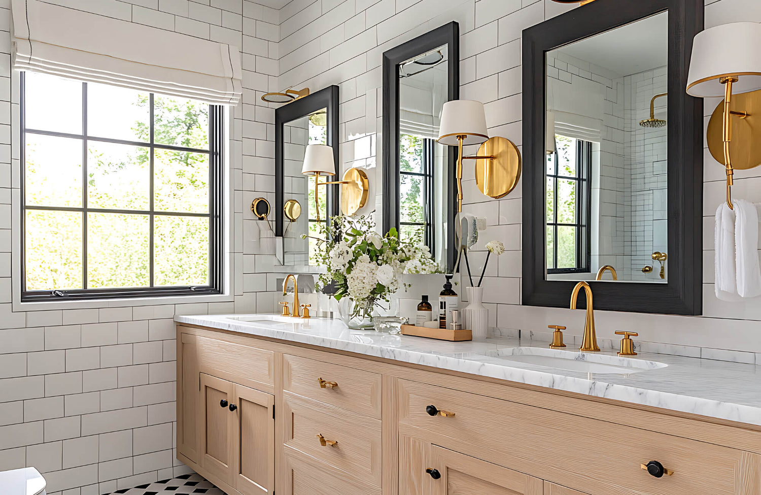 Bright and elegant bathroom with double vanity, gold fixtures, white subway tiles, and wall sconces beside framed mirrors.
