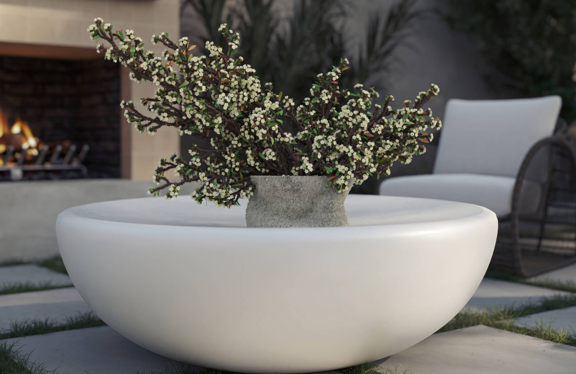 Outdoor lounge with sculptural round coffee table, floral arrangement, and soft neutral tones beside cozy fireplace seating.