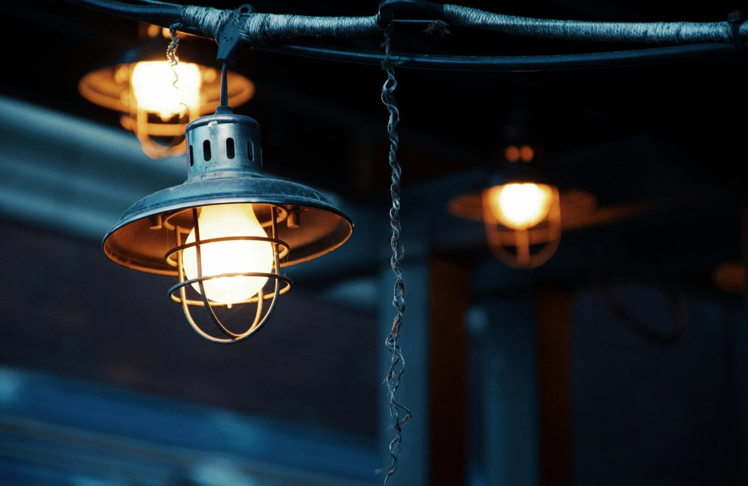 Close-up of a rustic metal cage pendant light glowing warmly against a dark, moody background.