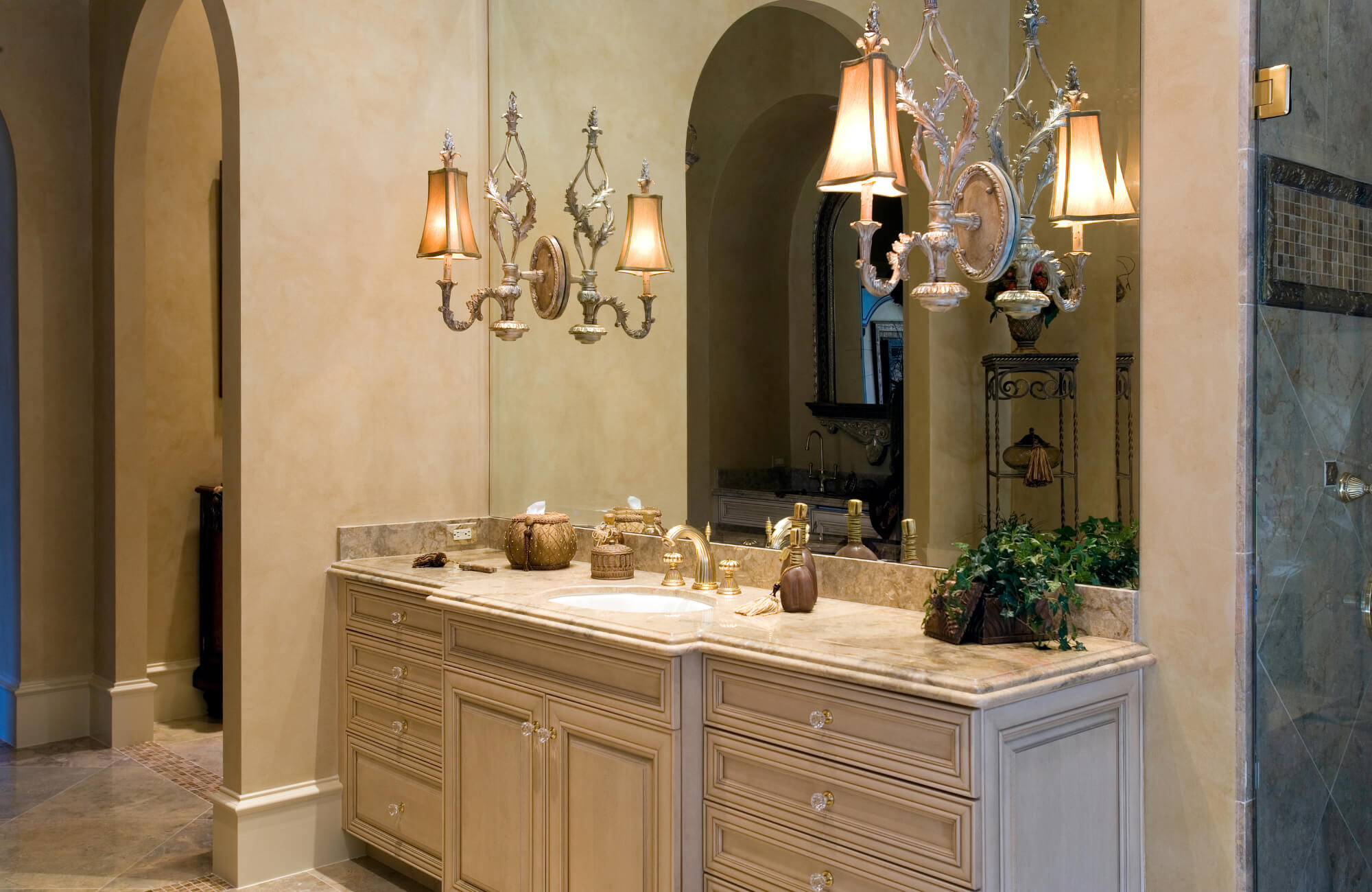 Elegant single-sink vanity with marble countertop, gold fixtures, ornate lighting, and ample drawer storage in a traditional bathroom setting.