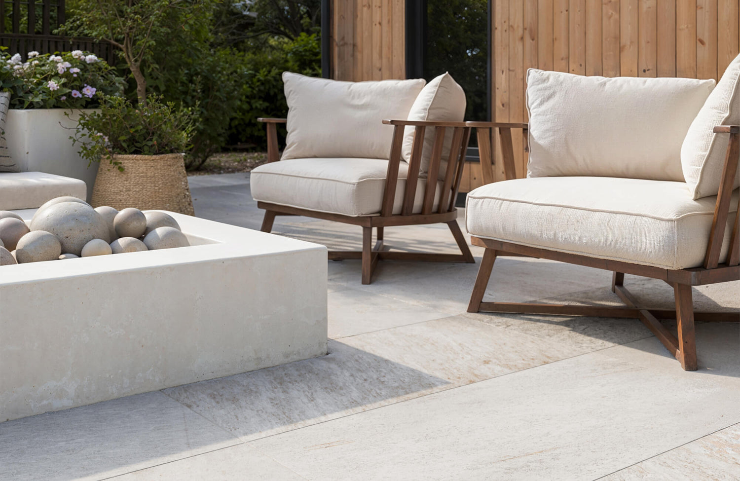 Close-up of pale porcelain patio tiles with wood-framed seating and sculptural fire pit, showing a clean, refined outdoor setup.