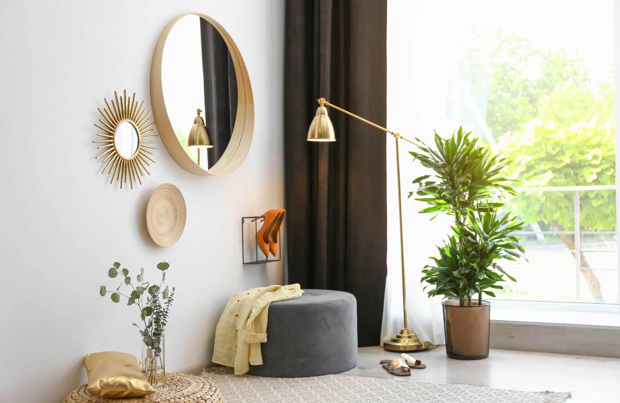 Modern living room corner with round and sunburst mirrors, gold floor lamp, potted plant, and cozy seating accents.