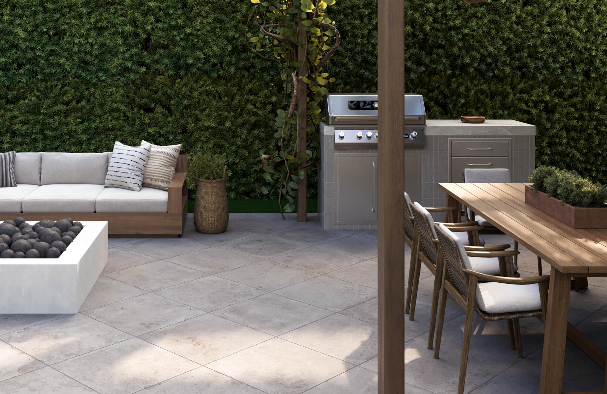 Spacious backyard setup featuring square porcelain pavers, a wooden dining table, outdoor grill, and sofa with neutral cushions set against a leafy backdrop.