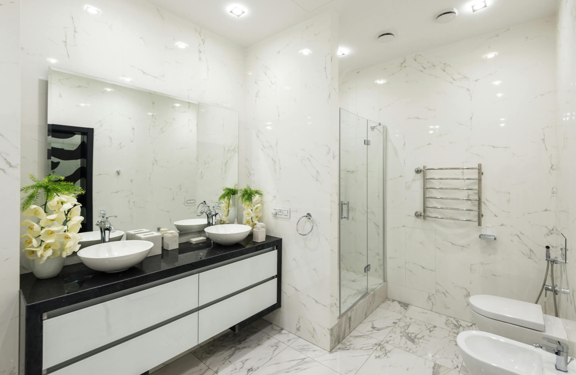 Luxurious bathroom with white marble walls and flooring, featuring a freestanding bathtub, black countertop, and double vessel sinks.