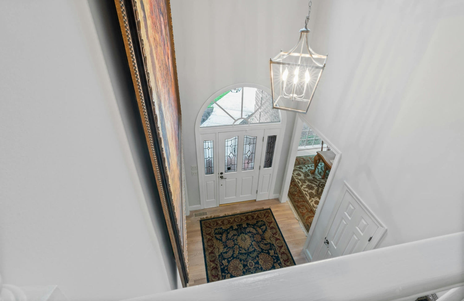 Bright foyer entry with a large lantern-style chandelier, arched glass door, and patterned rug creating a welcoming farmhouse-inspired space with natural light.