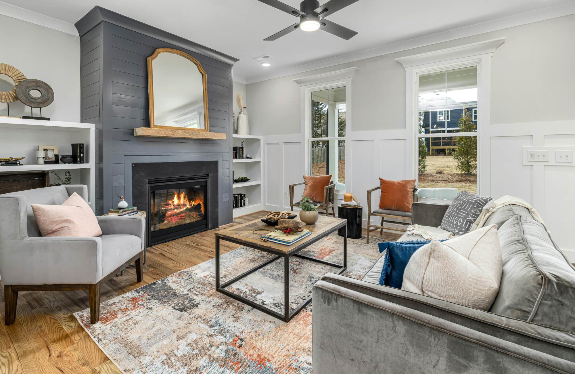 Transitional area rug in ivory, rust, and denim blue adds color and texture to a cozy living room with wood look flooring and a charcoal fireplace wall.