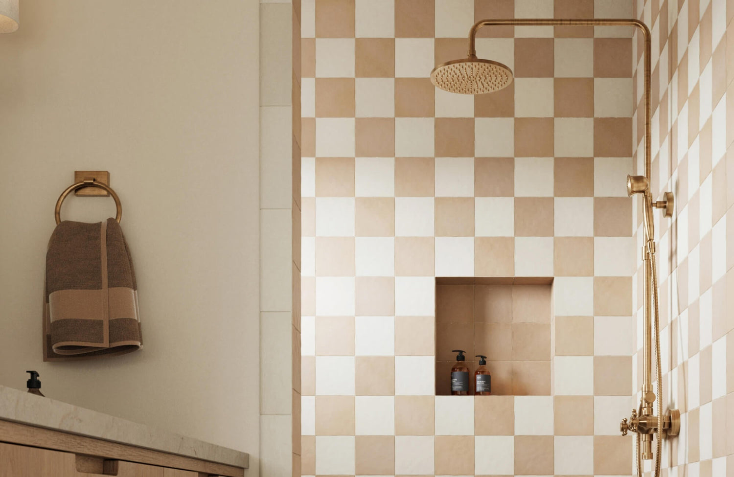 Shower with beige and white checkered tiles, brass fixtures, and a built-in niche, paired with a warm-toned vanity and towel ring for a cozy feel.