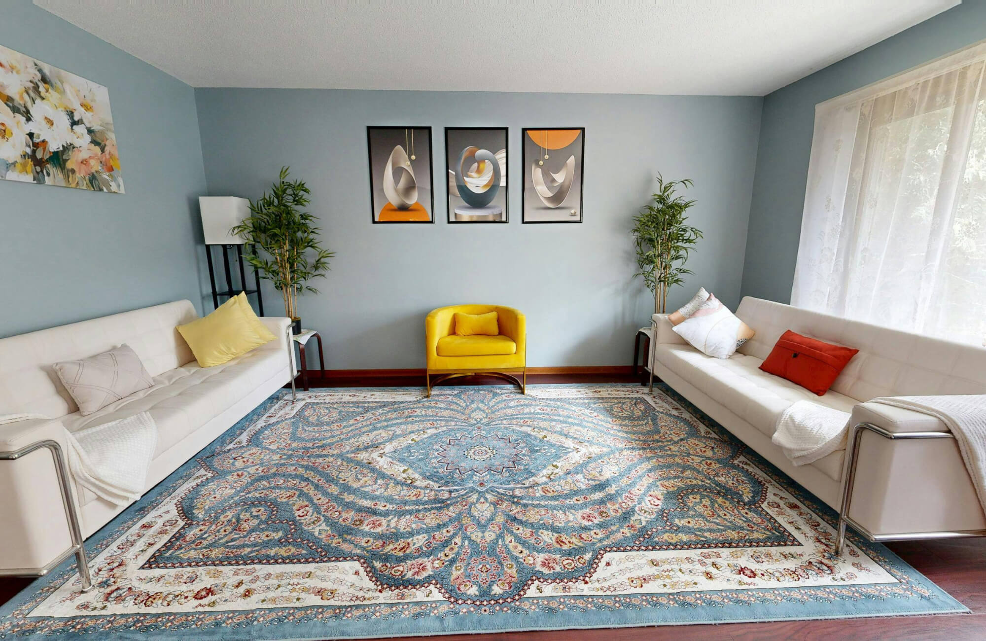 Open living room with two sofas and a yellow accent chair anchored by a large patterned rug that defines the seating area without walls.