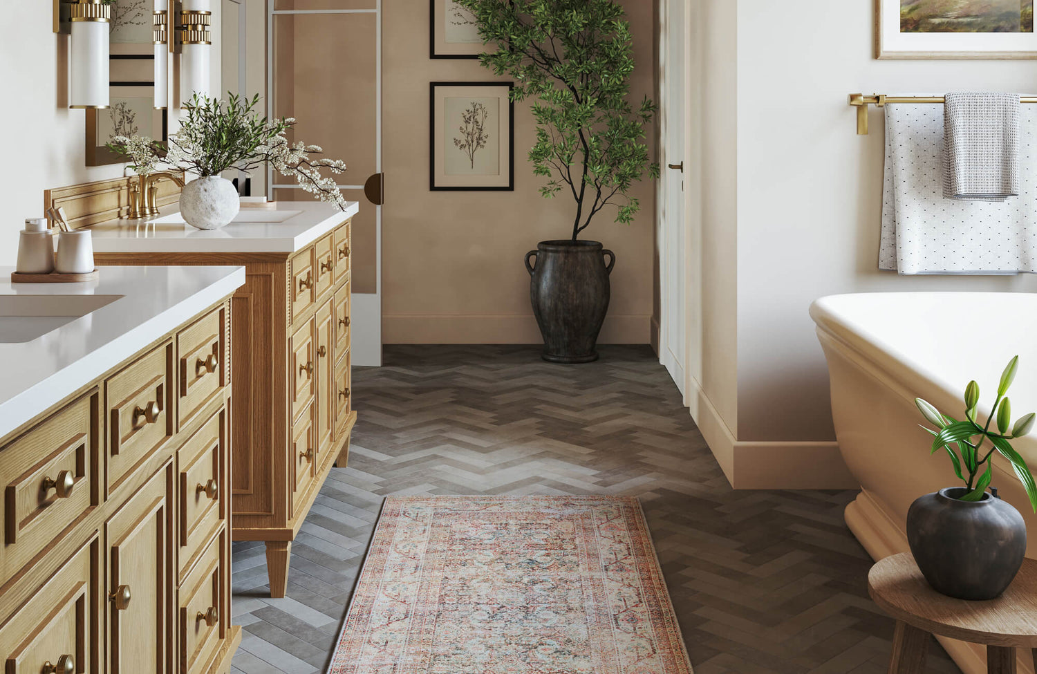 Warm, light-filled bathroom featuring twin wood vanities, white countertops, herringbone wood-look flooring, botanical artwork, and soft neutral walls, accented by a vintage-style runner, a freestanding tub, and greenery.