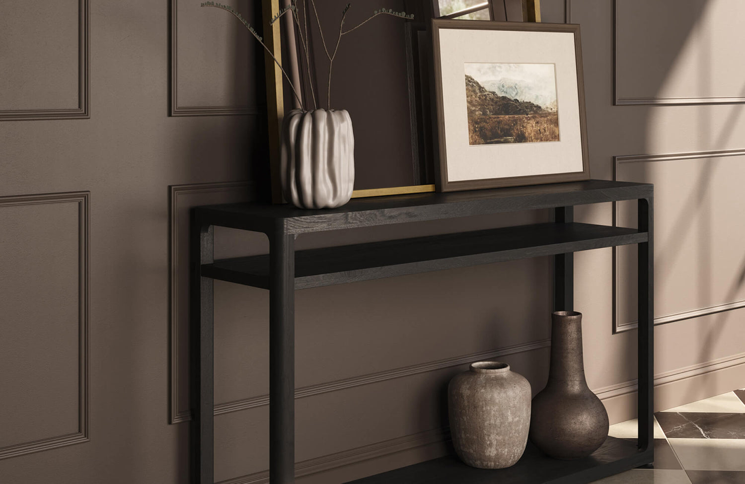 Framed landscape wall art in neutral tones displayed on a black console table with decorative vases against a paneled wall.