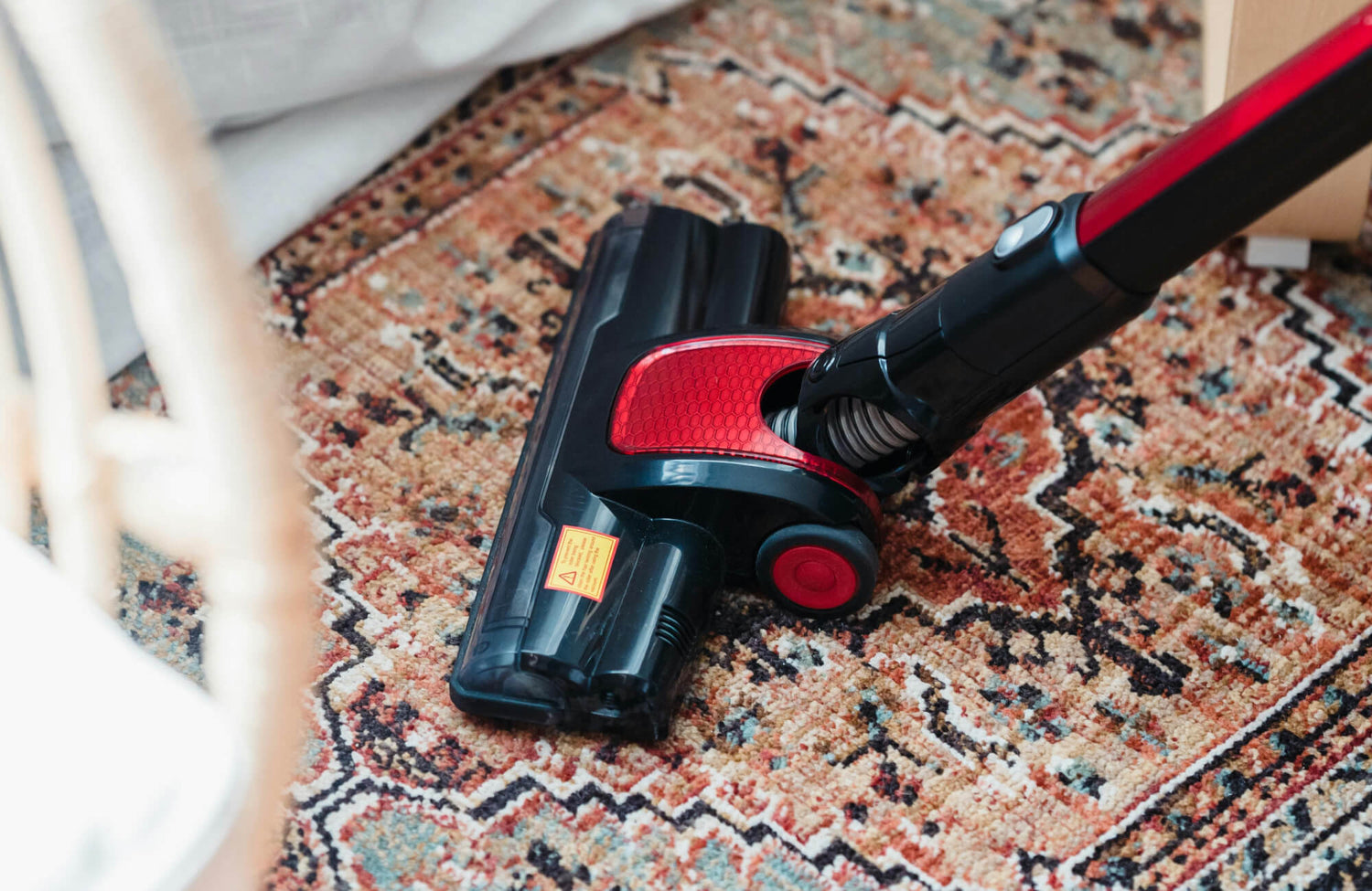 Close-up of a cordless vacuum cleaning a vintage-style rug with intricate patterns in warm earthy tones, enhancing a tidy living space.