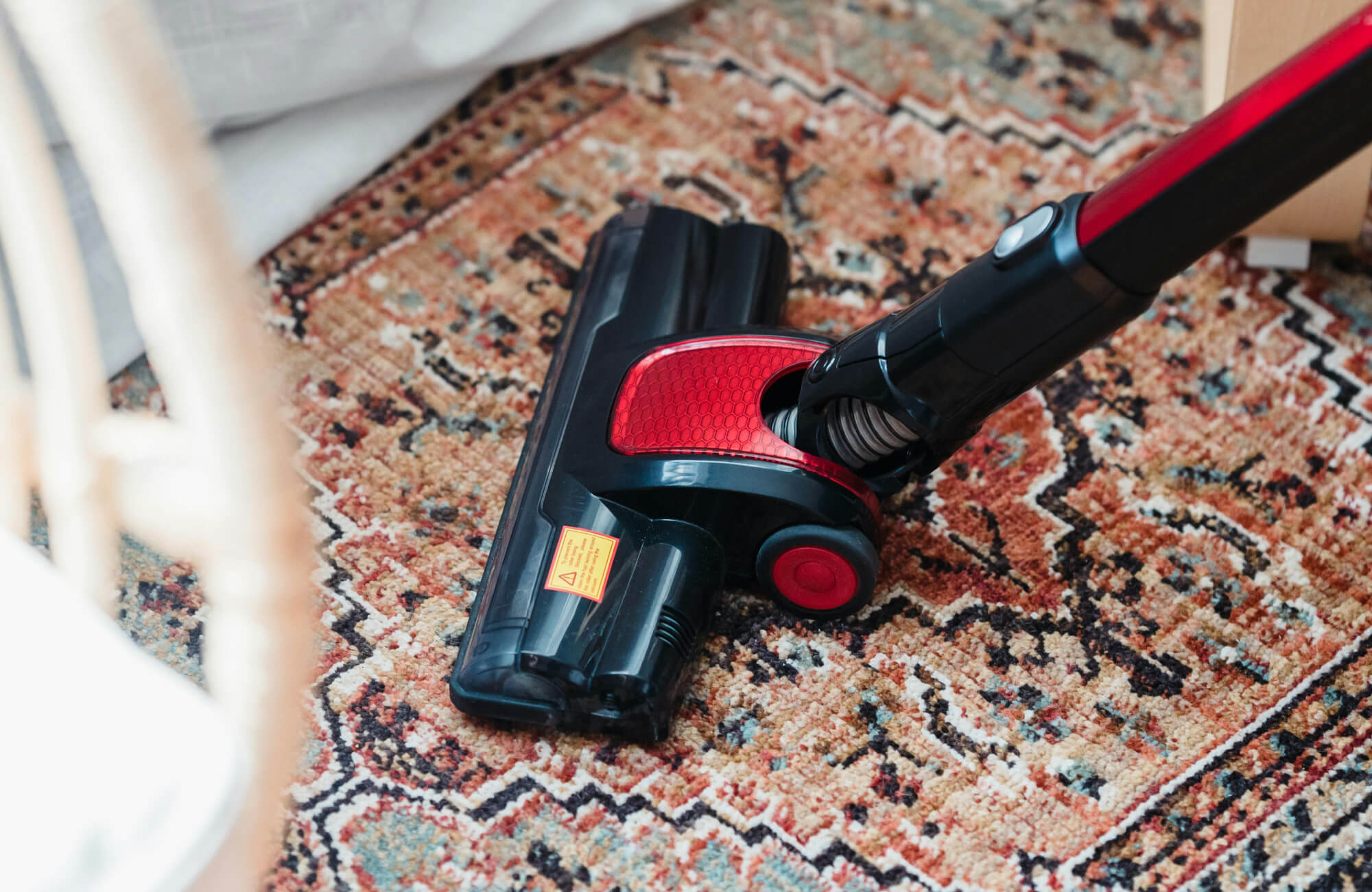 Close-up of a cordless vacuum cleaning a vintage-style rug with intricate patterns in warm earthy tones, enhancing a tidy living space.