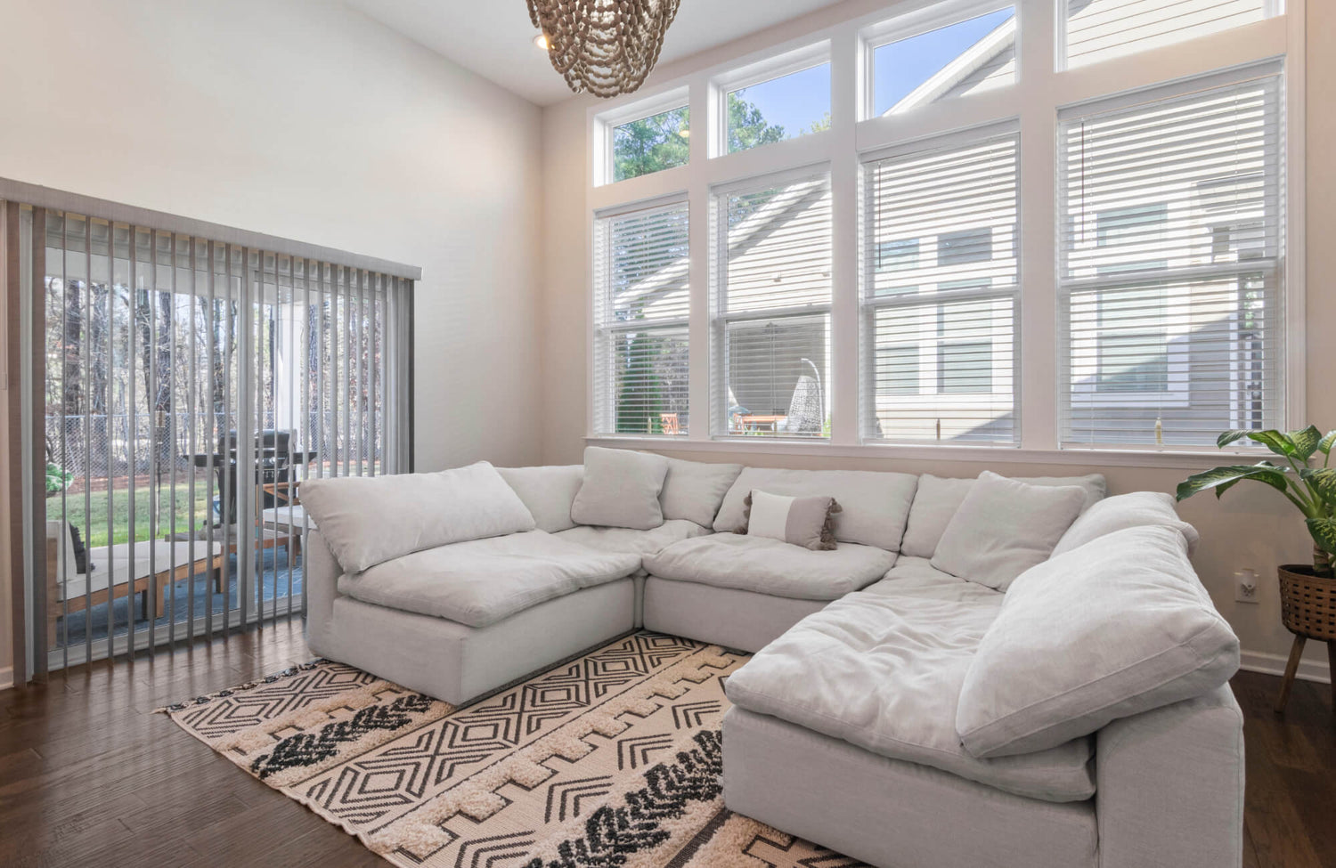 Bright living room with a large cream sectional sofa, patterned rug, tall windows, and wood floors creating a cozy, airy space.