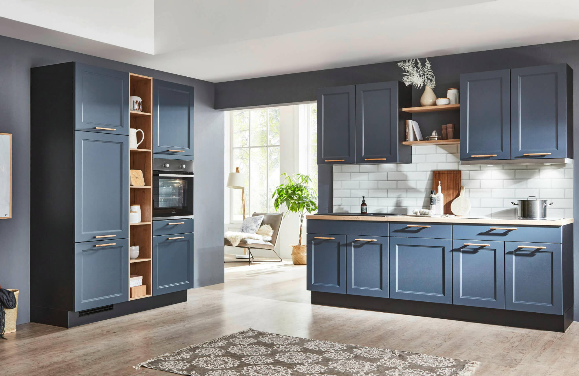 Modern kitchen with navy blue cabinets, wood accents, white subway backsplash, and a patterned rug runner on wood flooring.