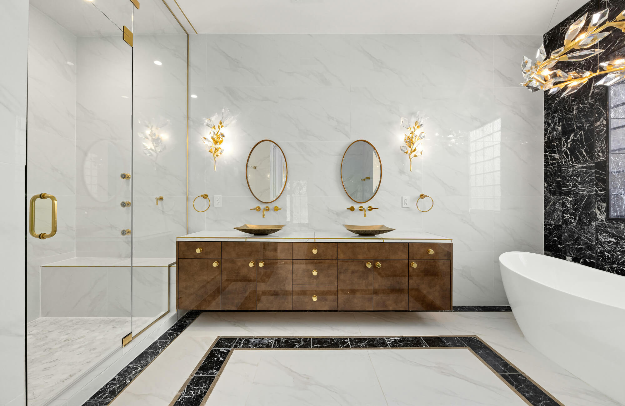 Modern white marble bathroom with gold framed round mirrors, brass fixtures, and a walnut double vanity.