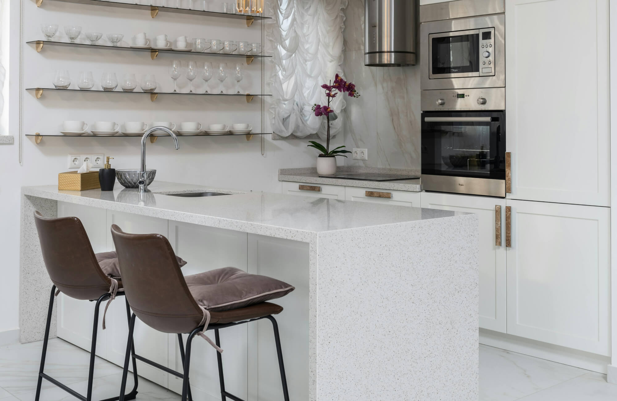 Kitchen island with stools showcased in a modern kitchen featuring a polished white waterfall-edge island, sleek leather counter stools with plush cushions, and open glass shelving.
