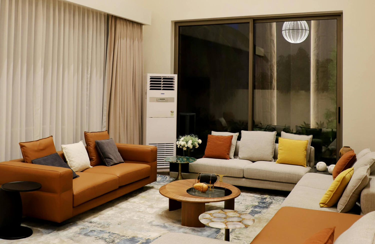Contemporary living room with caramel leather sofas, decorative pillows, center table, and expansive black-framed windows.