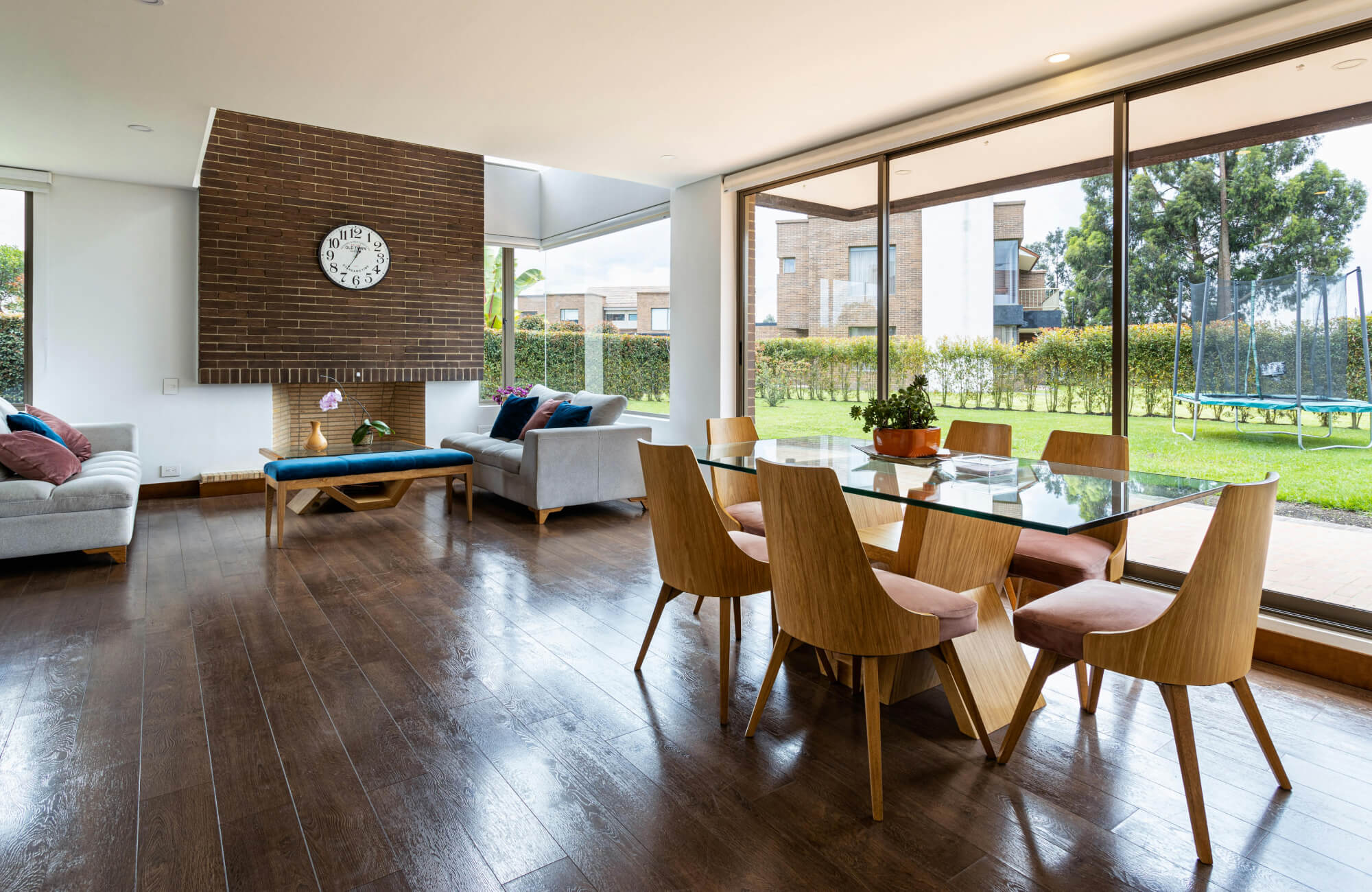 Modern living space featuring beige wood-look floor tiles complemented by a brown leather sofa, black pedestal side table, and neutral patterned rug.