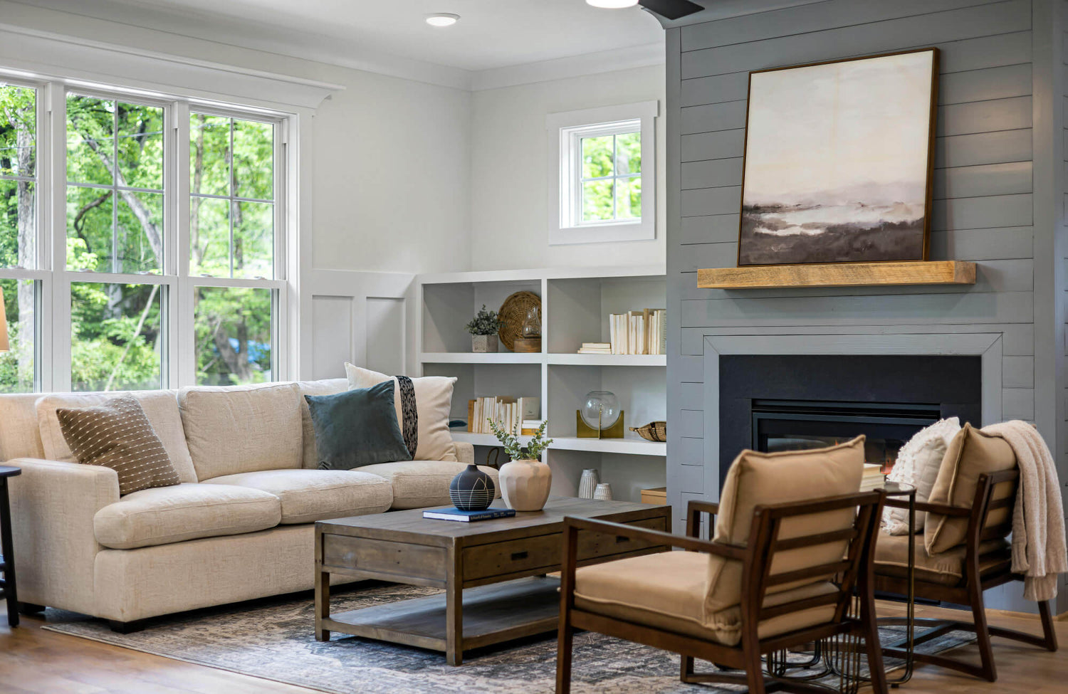 Contemporary living room with neutral tones, fireplace feature wall, built-in shelves, and cozy couch with throw pillows.