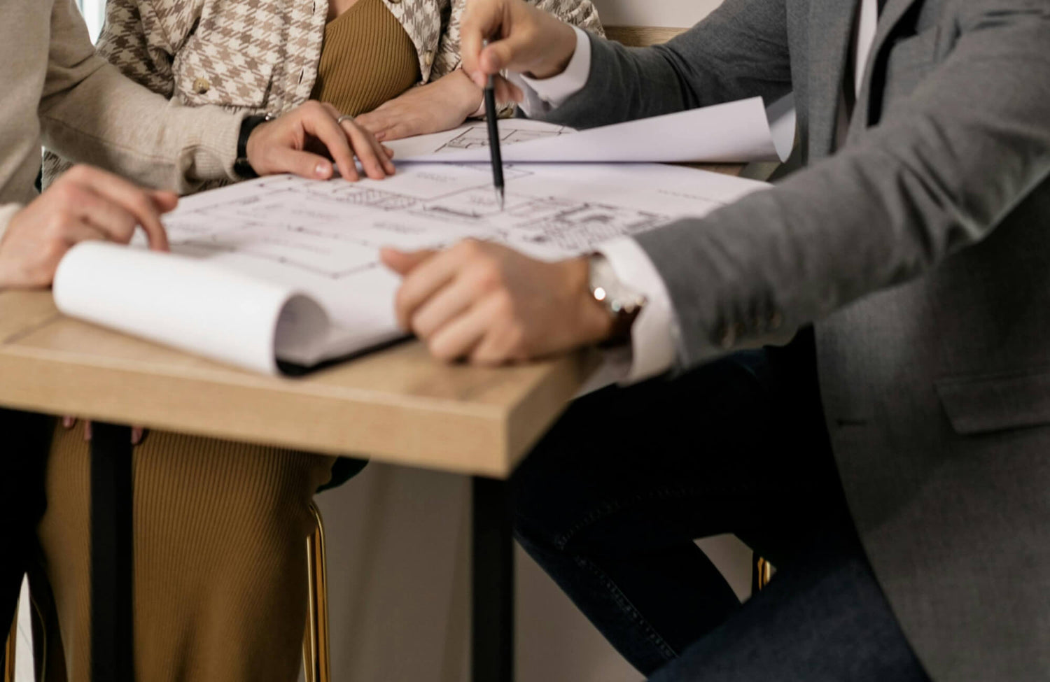 A close-up scene shows people reviewing architectural floor plans together at a small table, highlighting collaborative planning and decision-making essential for a smooth bathroom renovation.