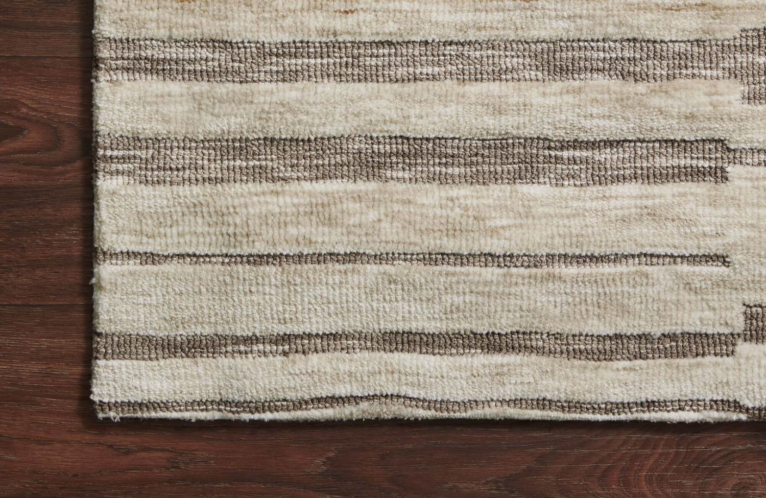 Close-up of the Rollins Polyester Pile Rug in Sand and Espresso, featuring striped patterns, laid over dark wood flooring