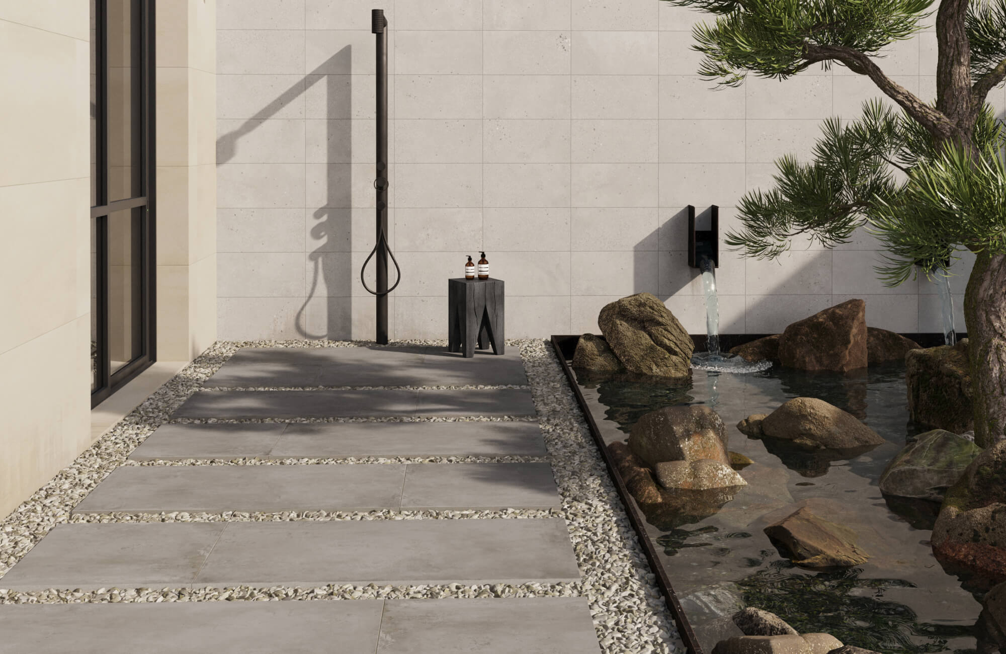 Porcelain pavers laid in a minimalist patio with a black outdoor shower, gravel accents, and a stone water feature bordered by sculptural greenery.