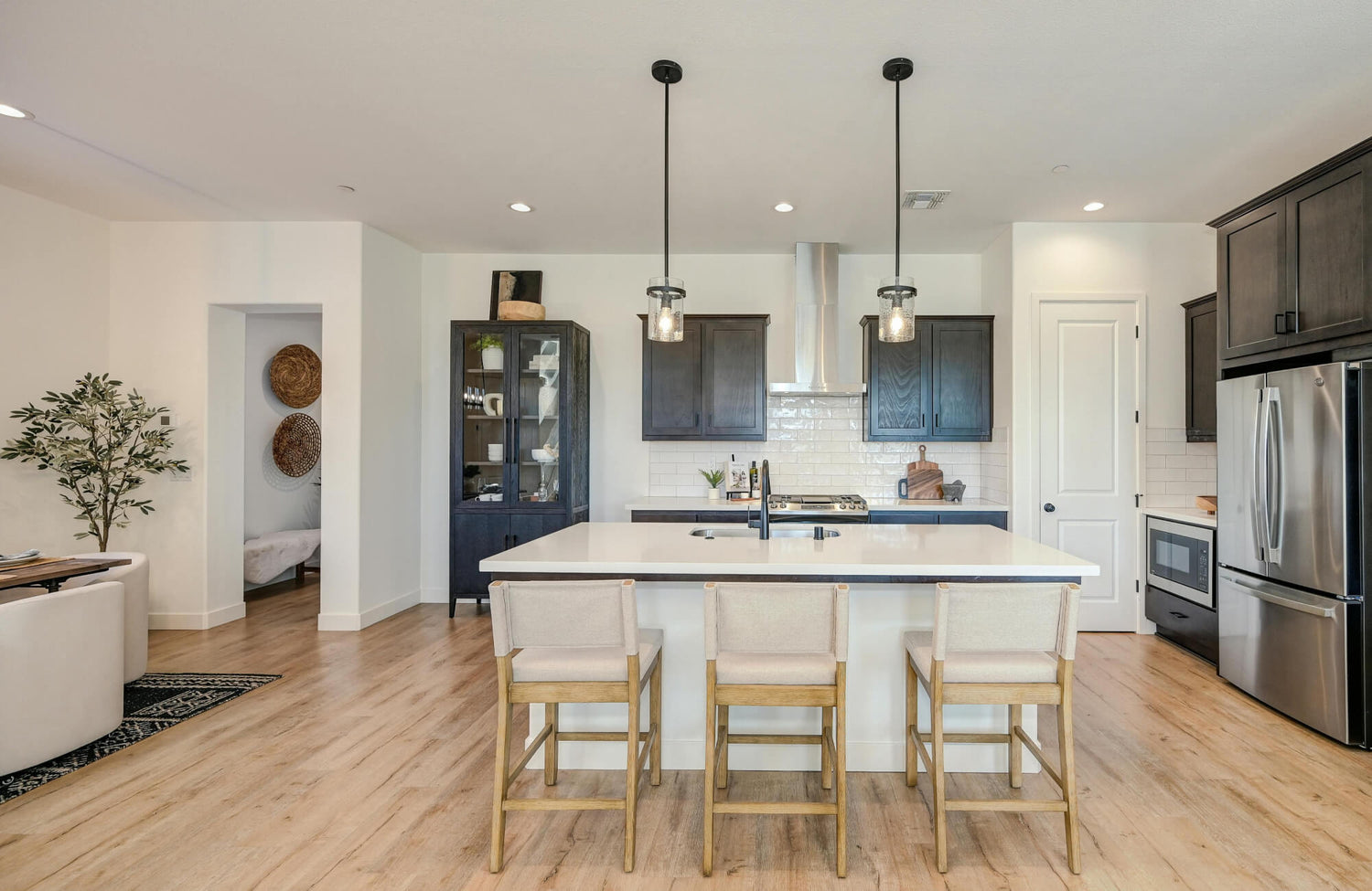Black metal pendants hang above a bright kitchen island with light wood floors and upholstered stools.