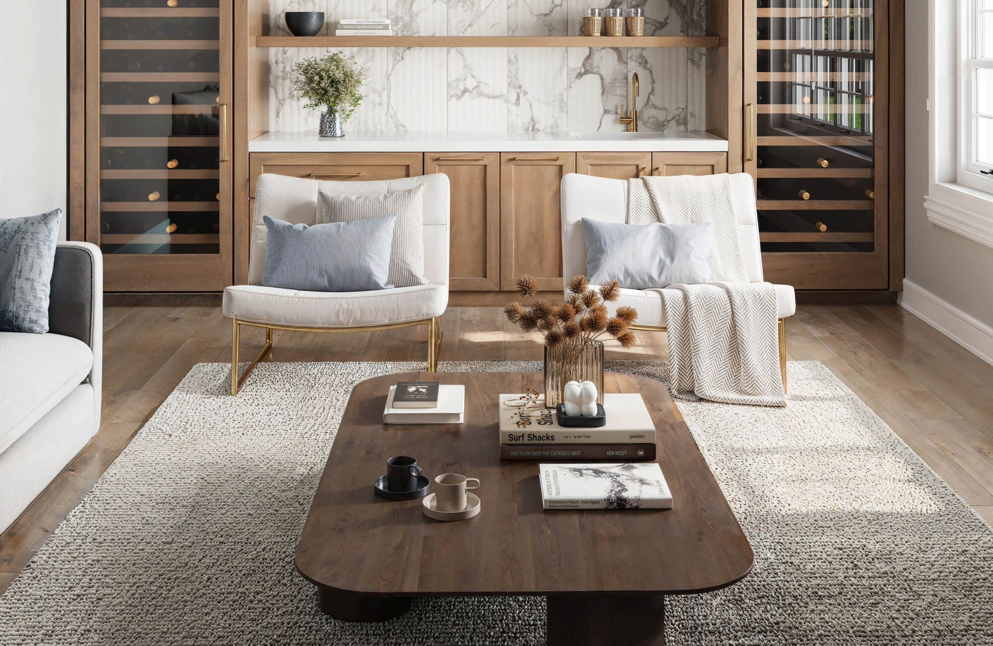 Elegant sitting area with cozy seating, a rich wood coffee table, and a plush neutral rug complementing the marble-accented wet bar and wine storage.