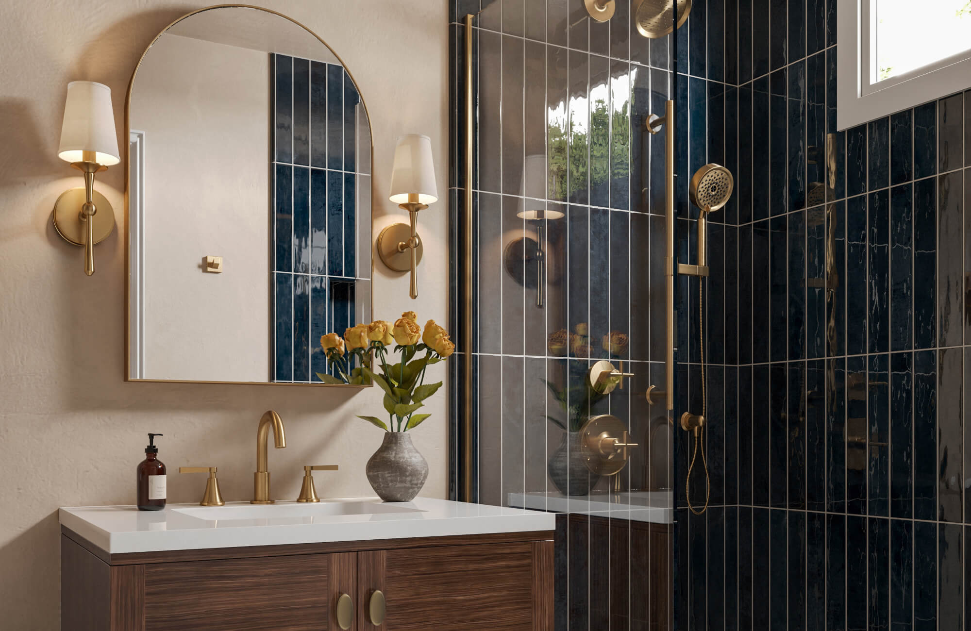 Brass wall sconces with white shades frame a gold-trimmed arch mirror above a wood vanity with a white solid surface top, set against navy vertical tile and a glass shower.