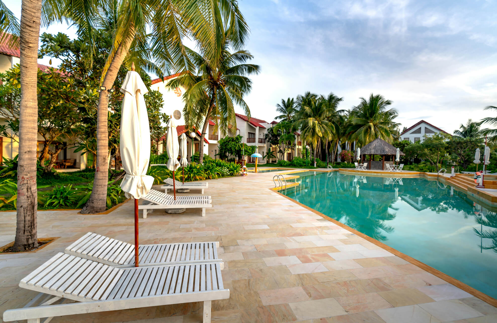 Resort-style swimming pool with porcelain paver flooring, shaded seating, and lush greenery creating a relaxing atmosphere.