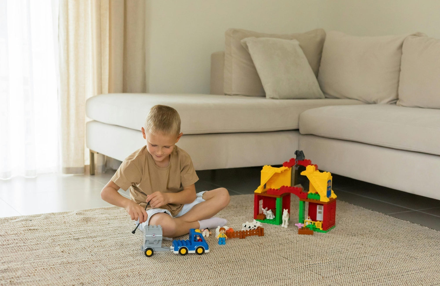A young boy plays with toy trucks and a colorful building set on a textured beige rug, creating a cozy and inviting play area.