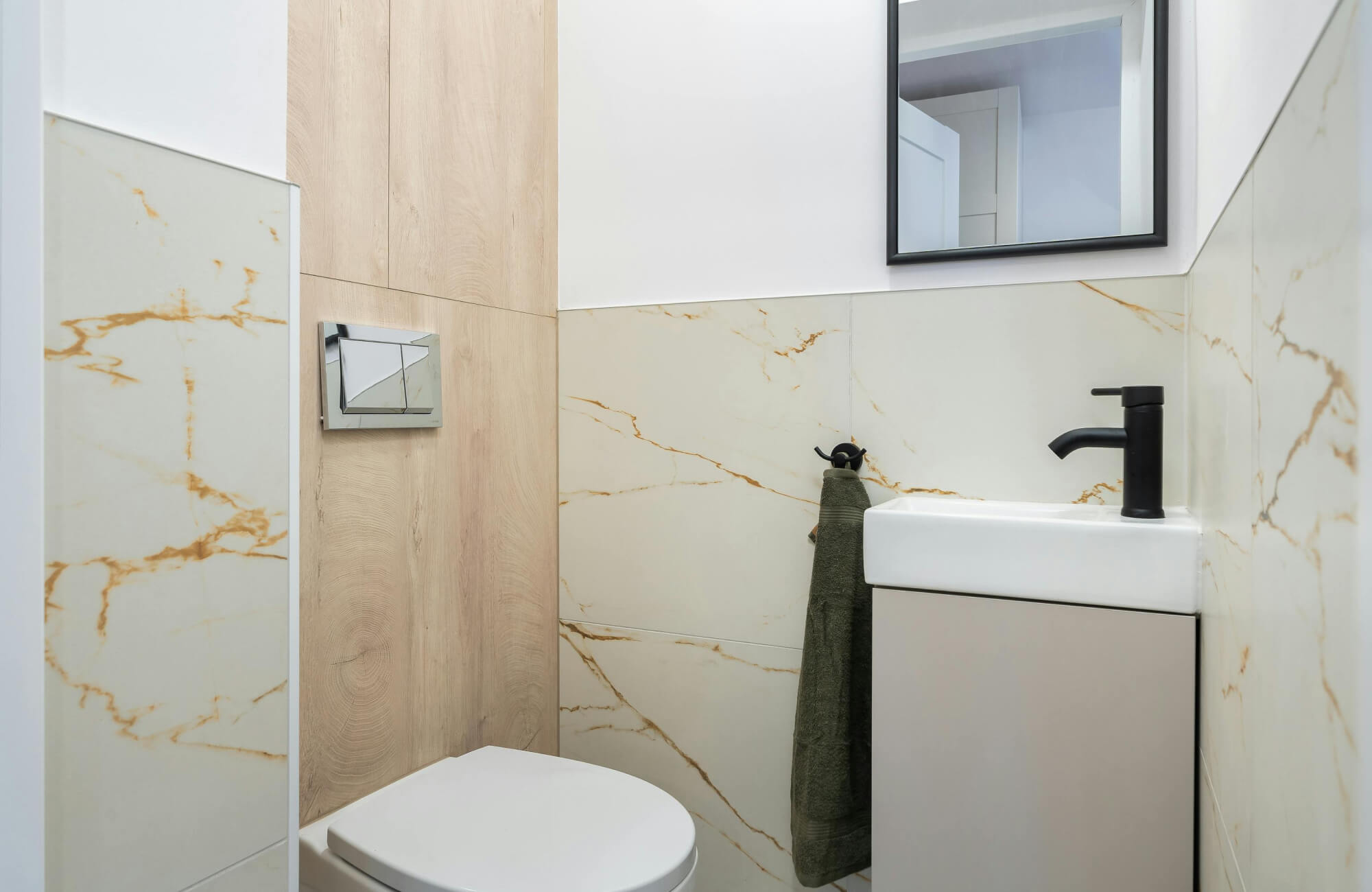 Small bathroom layout featuring a narrow vanity with integrated sink, marble-inspired wall tiles, and warm wood tones for visual balance.