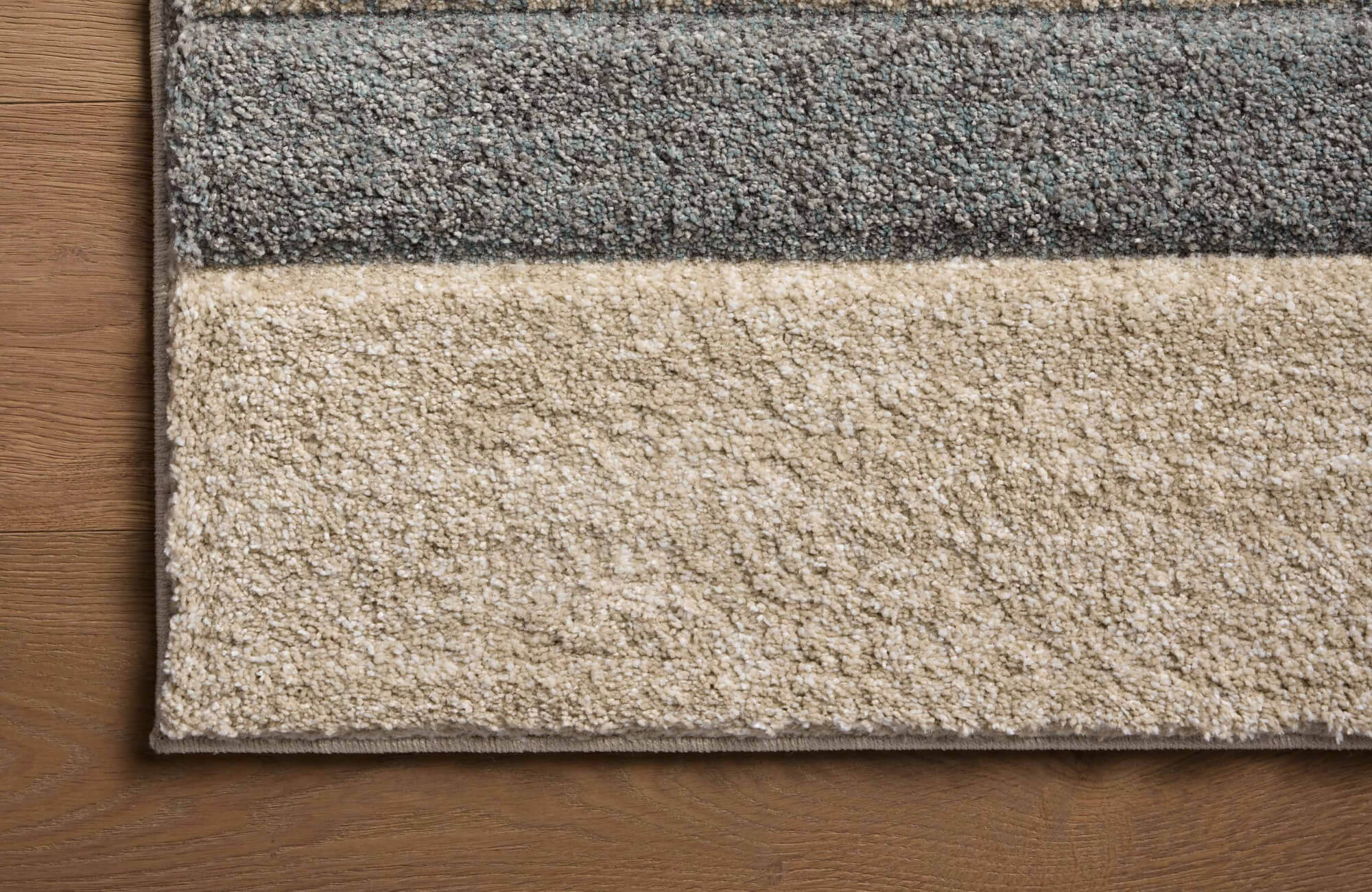 Close-up of a textured polypropylene rug with soft gray and beige bands, highlighting dense pile and durable woven construction.