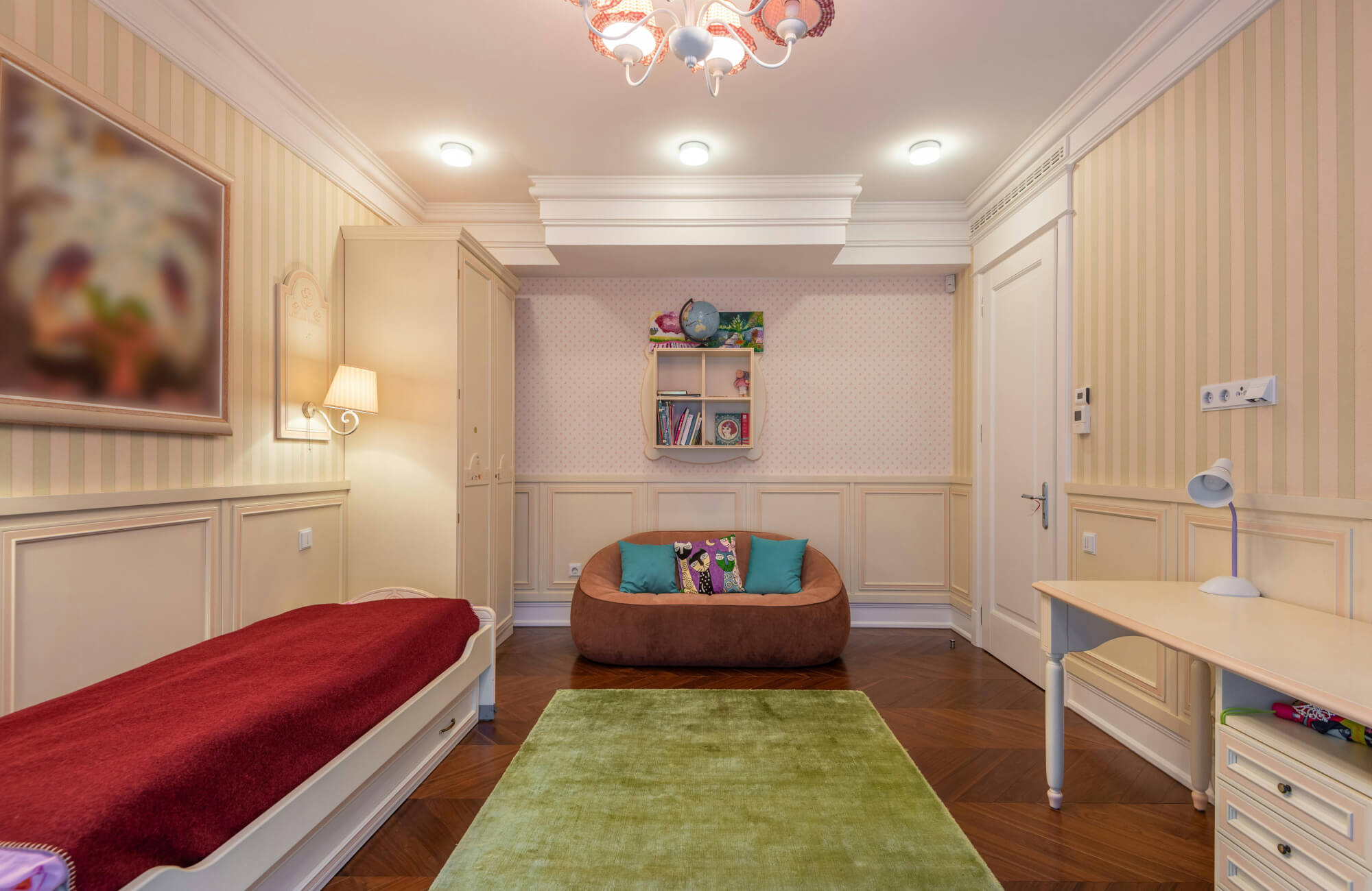 A cozy kids’ room featuring a soft green rug, a brown beanbag-style sofa with colorful pillows, built-in shelving with books and toys, and warm striped walls that create a calm, playful space.
