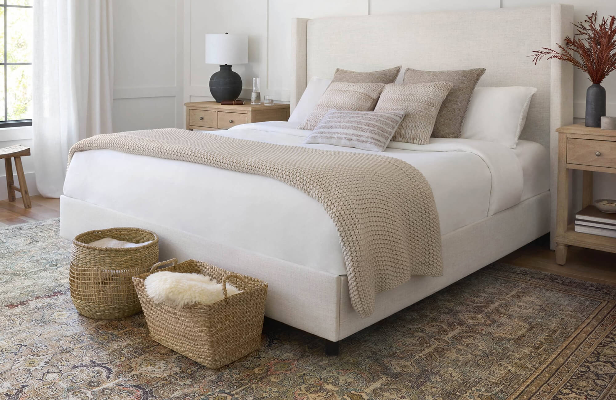 Elegant bedroom featuring a textured area rug in soft beige and sage hues, woven baskets, and a plush neutral-toned bed setup.