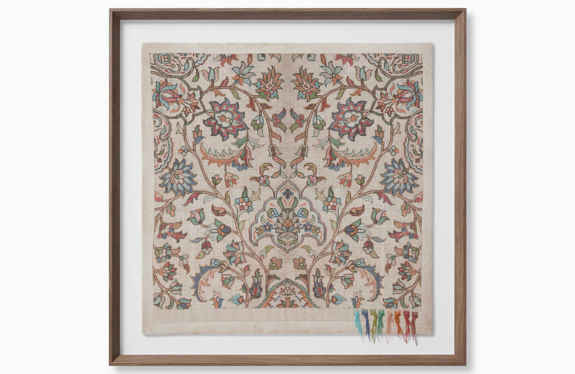 Framed textile wall art with a floral pattern, muted blue, coral, green, and beige embroidery, and a warm wood frame against a white background.