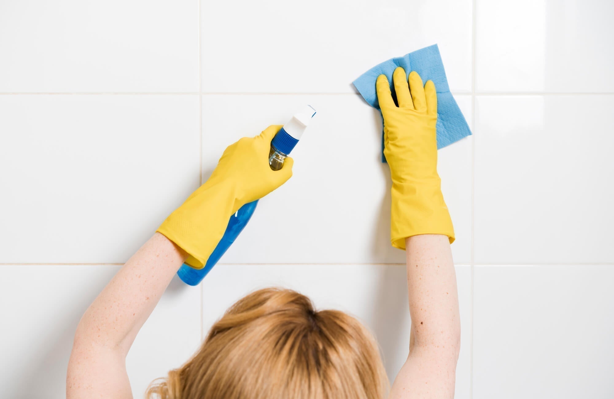 Person cleaning a ceramic tile backsplash with a spray bottle and cloth, highlighting its easy-to-maintain surface.