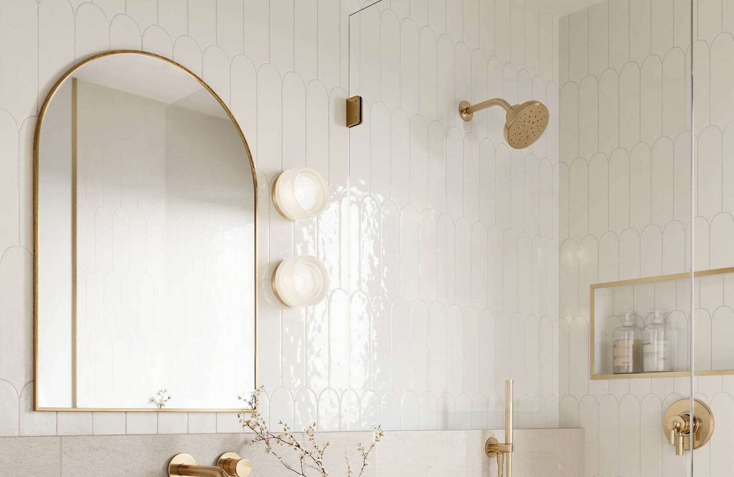 Bathroom with white scallop ceramic wall tile, arched brass mirror, and brushed gold fixtures creating a refined spa-inspired look