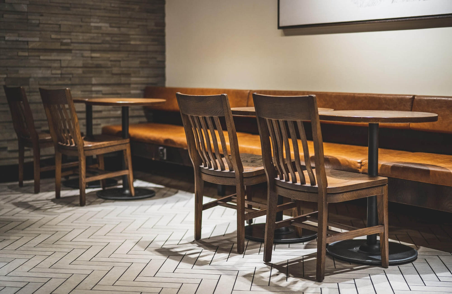 Cozy café interior with warm wood chairs, leather banquette seating, and sleek herringbone floor tile adding modern texture to the space.