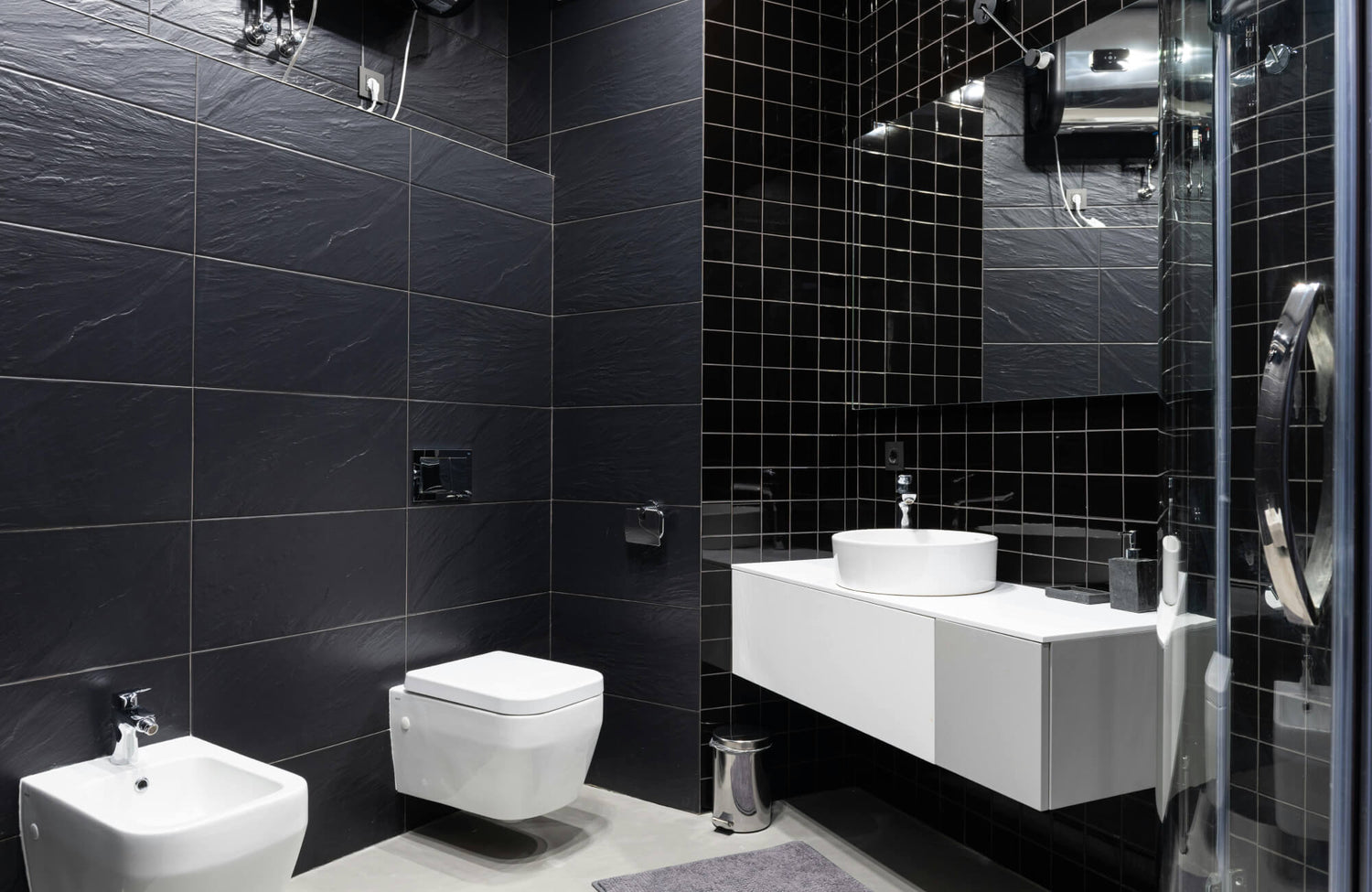 Modern bathroom with large matte black wall tiles and glossy black square tiles, contrasted by a white floating vanity and fixtures for a sleek, balanced look.