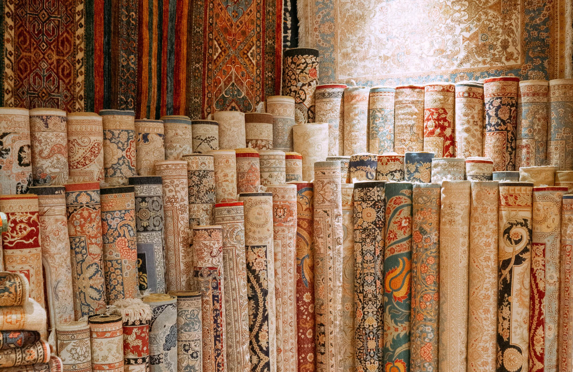 A layered collection of rolled vintage rugs with ornate motifs and faded textures, highlighting the variety of colors and traditional designs.